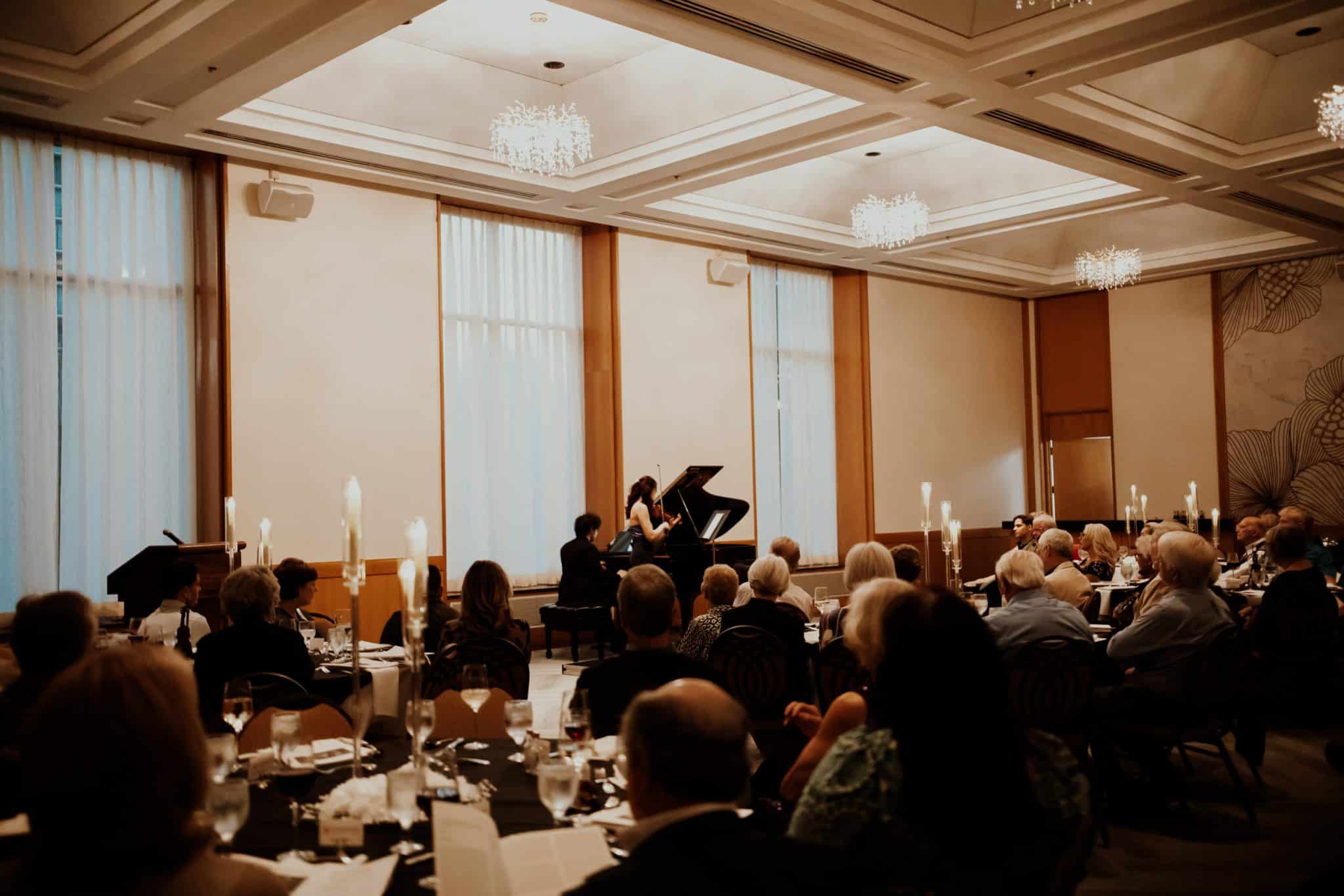A violinist and pianist perform in front of an audience.