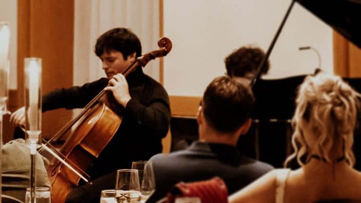 A cellist plays in front of a grand piano.